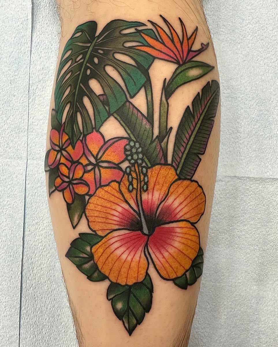 Traditional tropical tattoo on a leg featuring an orange hibiscus and monstera leaves