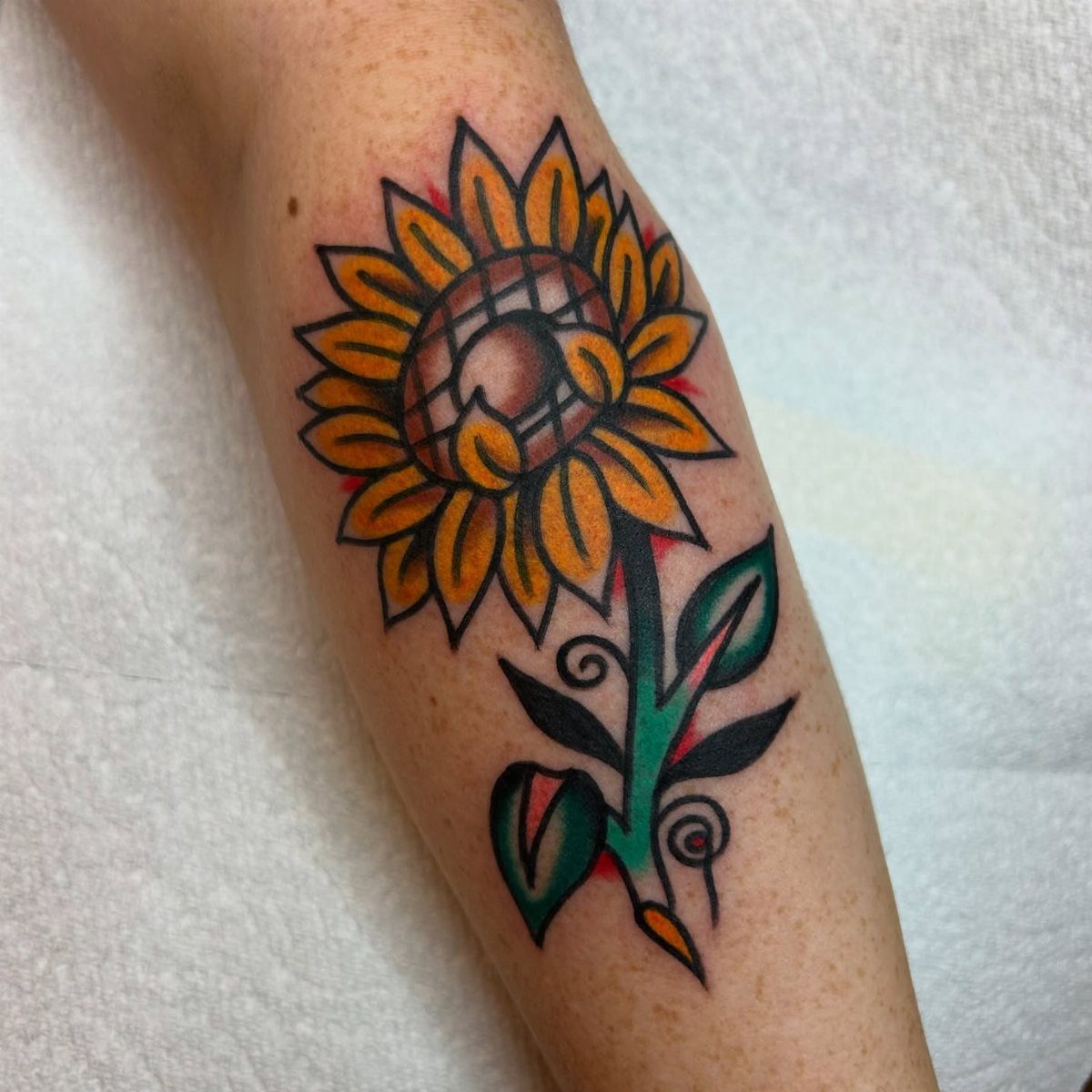 Traditional yellow sunflower tattoo with green leaves on a person's forearm