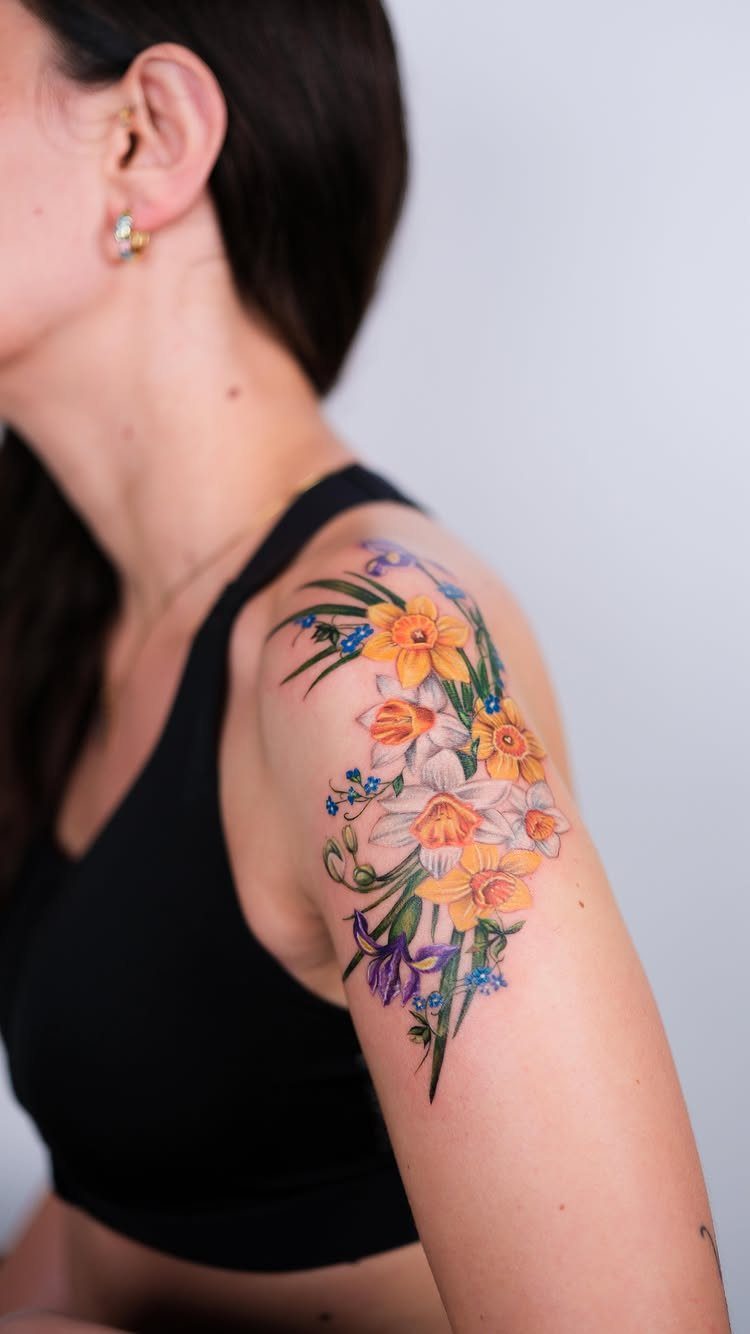 Yellow and white daffodil tattoo with purple flowers on a woman's shoulder