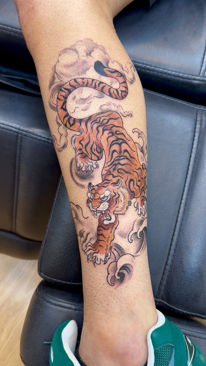 Japanese style tiger tattoo with clouds and waves on a person's lower leg