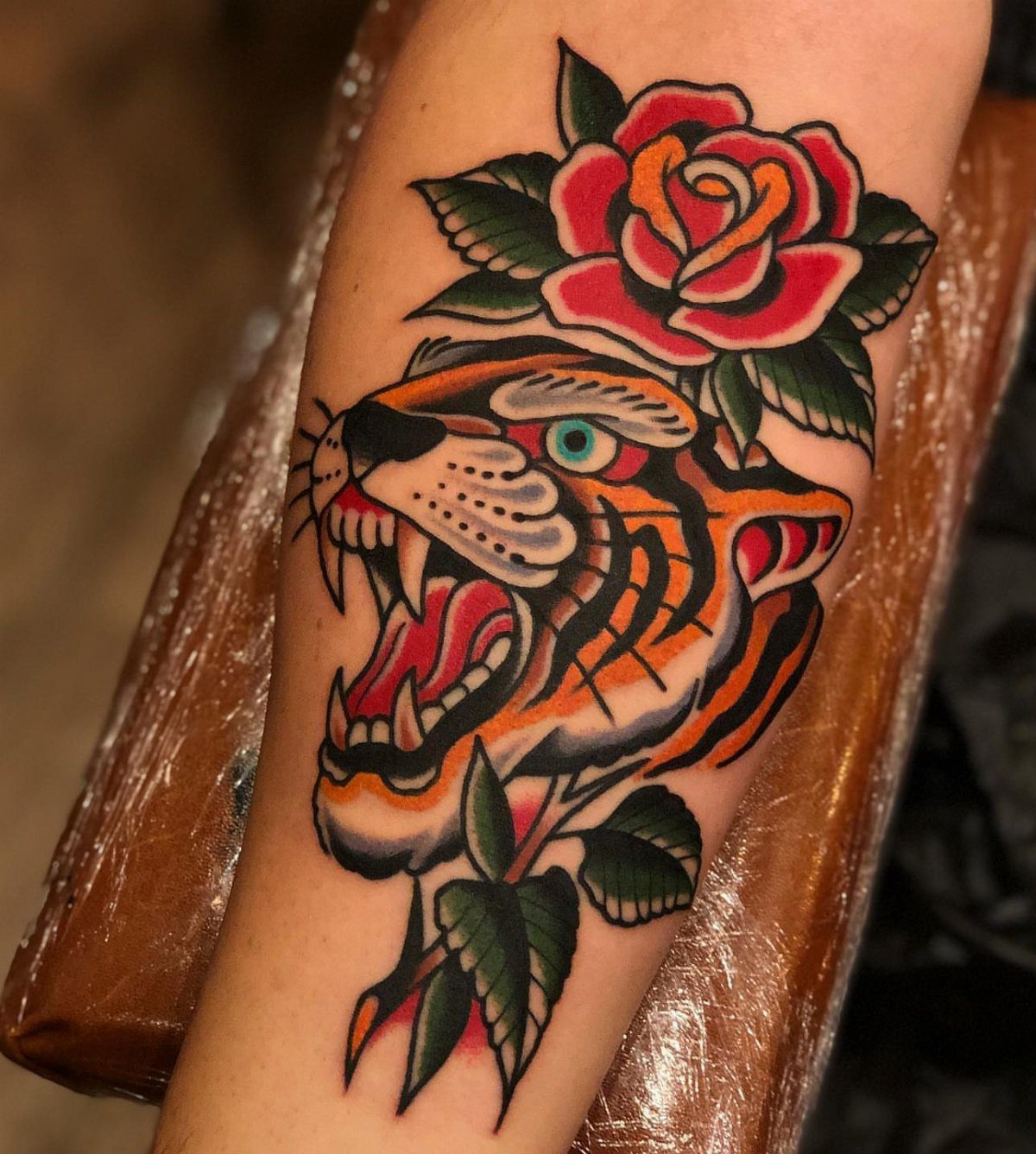 Traditional tiger head tattoo with red roses on a person's forearm