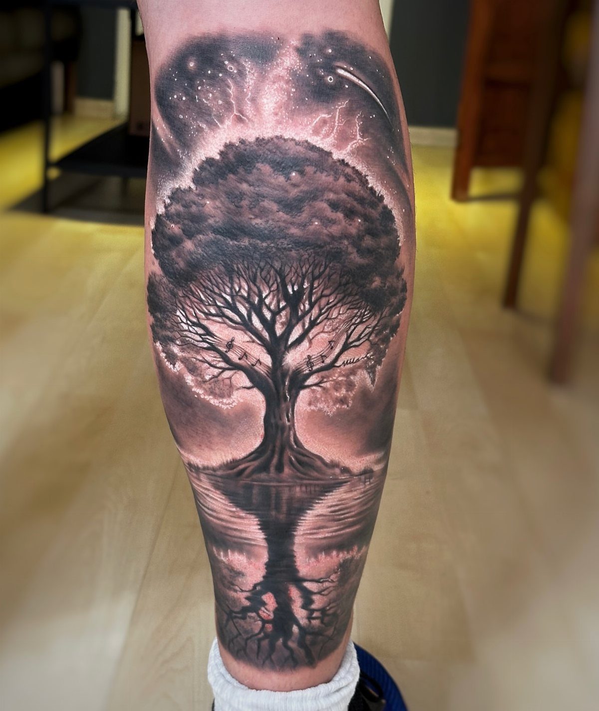 Tree of life tattoo on a leg with cosmic sky and water reflection.