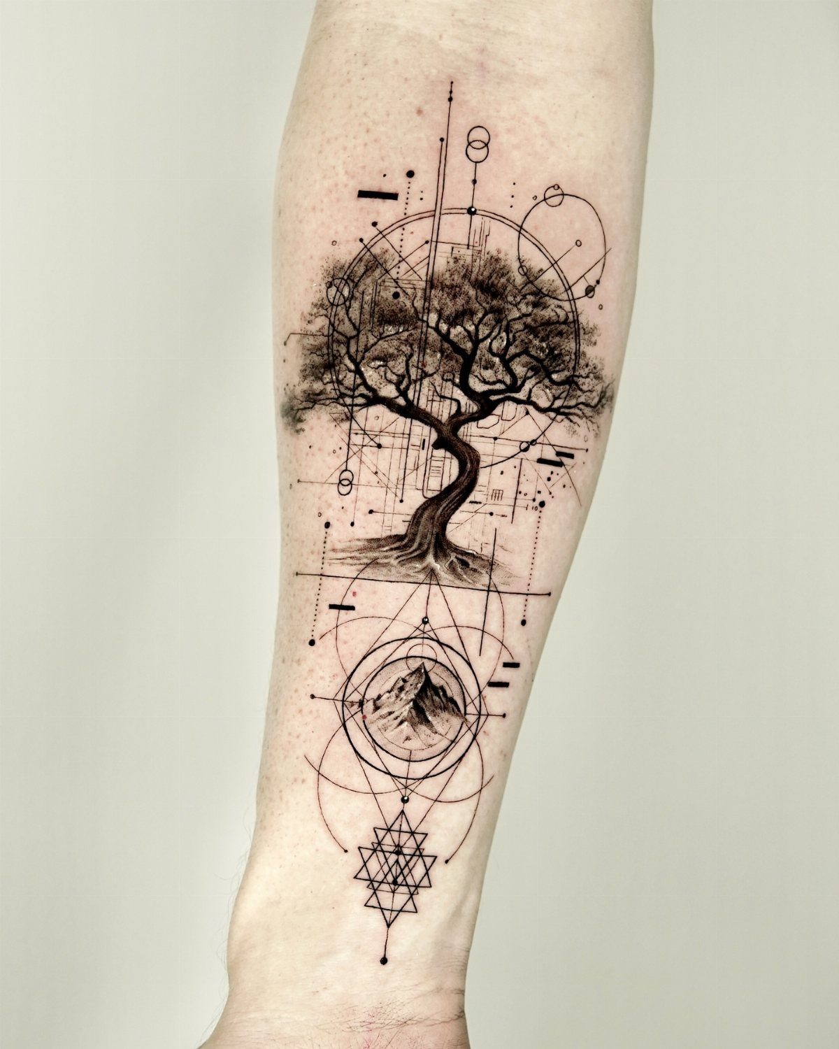 Geometric tree of life tattoo on a forearm with mountains and sacred geometry.