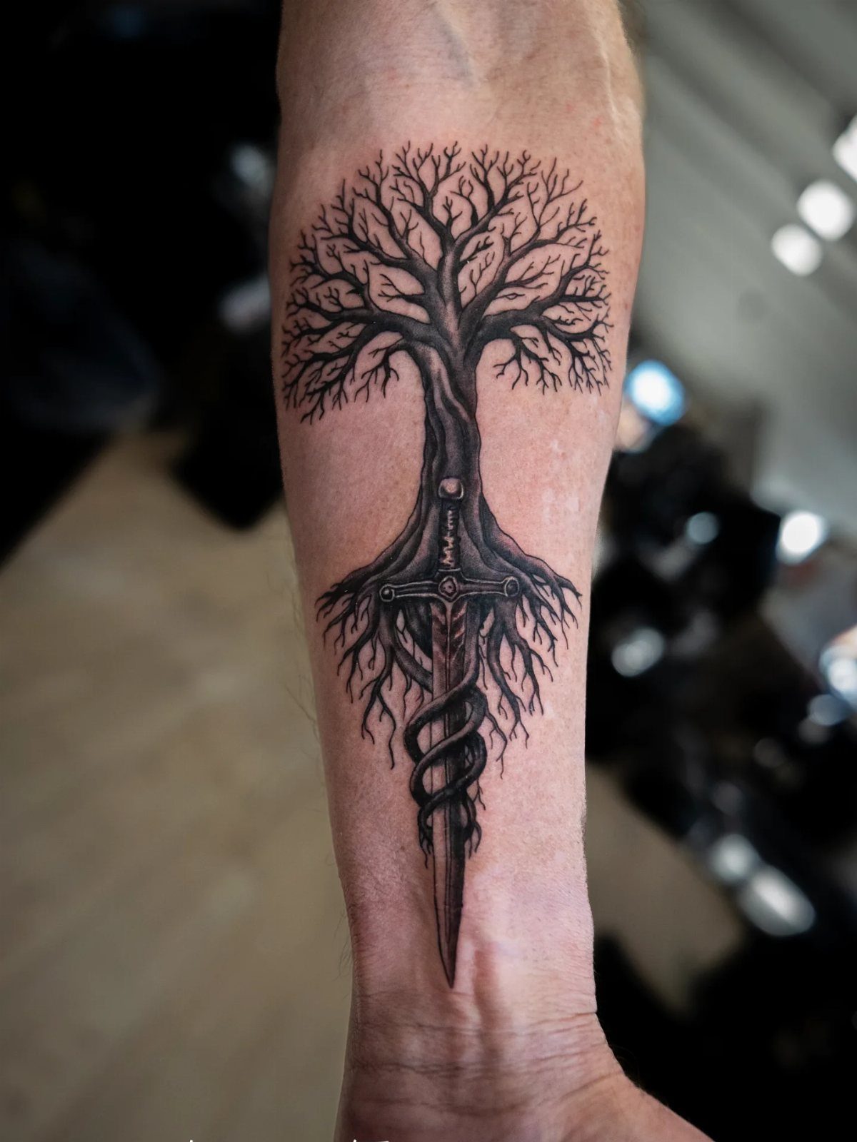 Tree of life tattoo on a forearm featuring a sword and a snake.