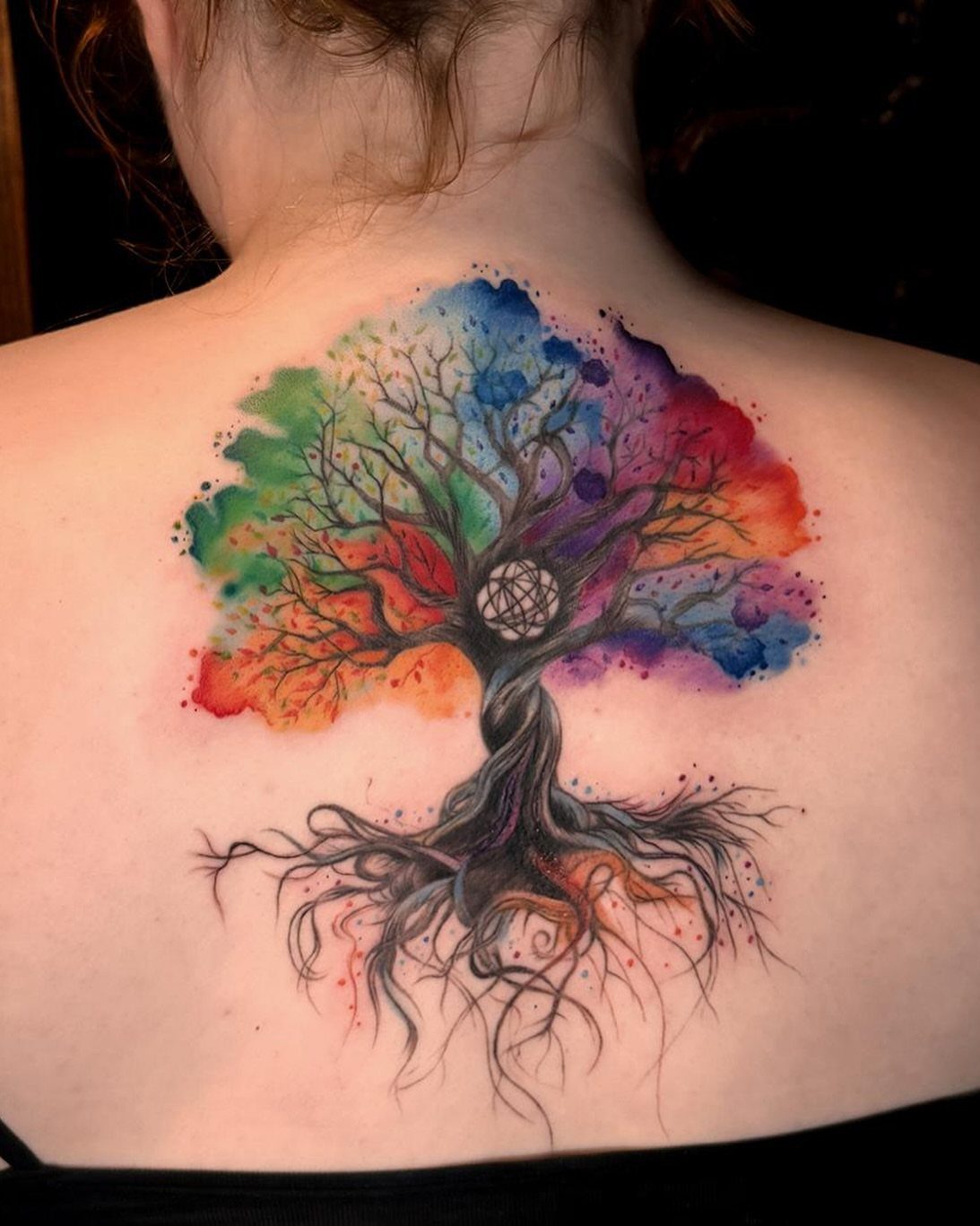 Watercolor tree of life tattoo on a person's back with vibrant colorful canopy