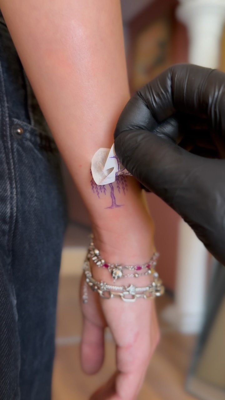 Small purple weeping willow tree tattoo on a wrist being cleaned with cotton.