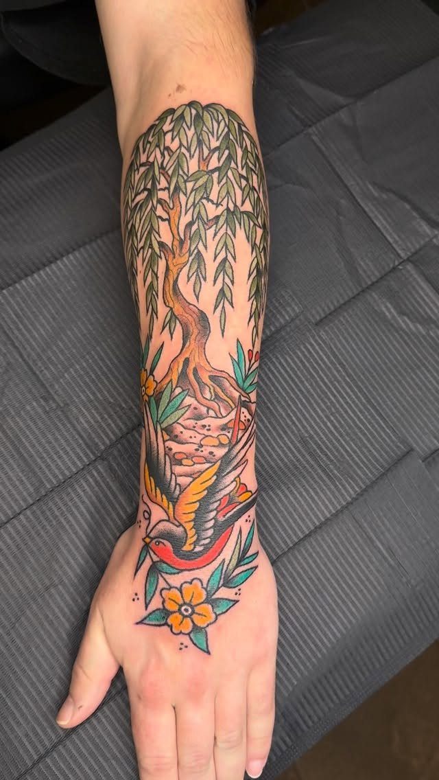 Weeping willow tree tattoo on a forearm with a bird and yellow flowers.