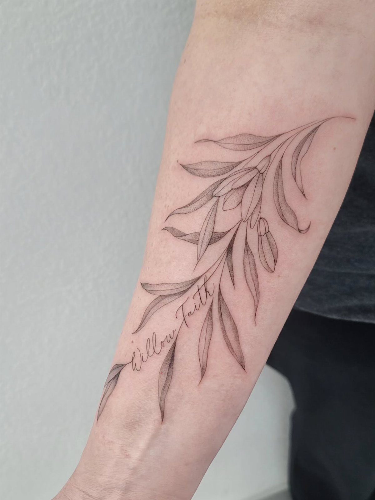 Willow branch tattoo with leaves and cursive text on a person's forearm