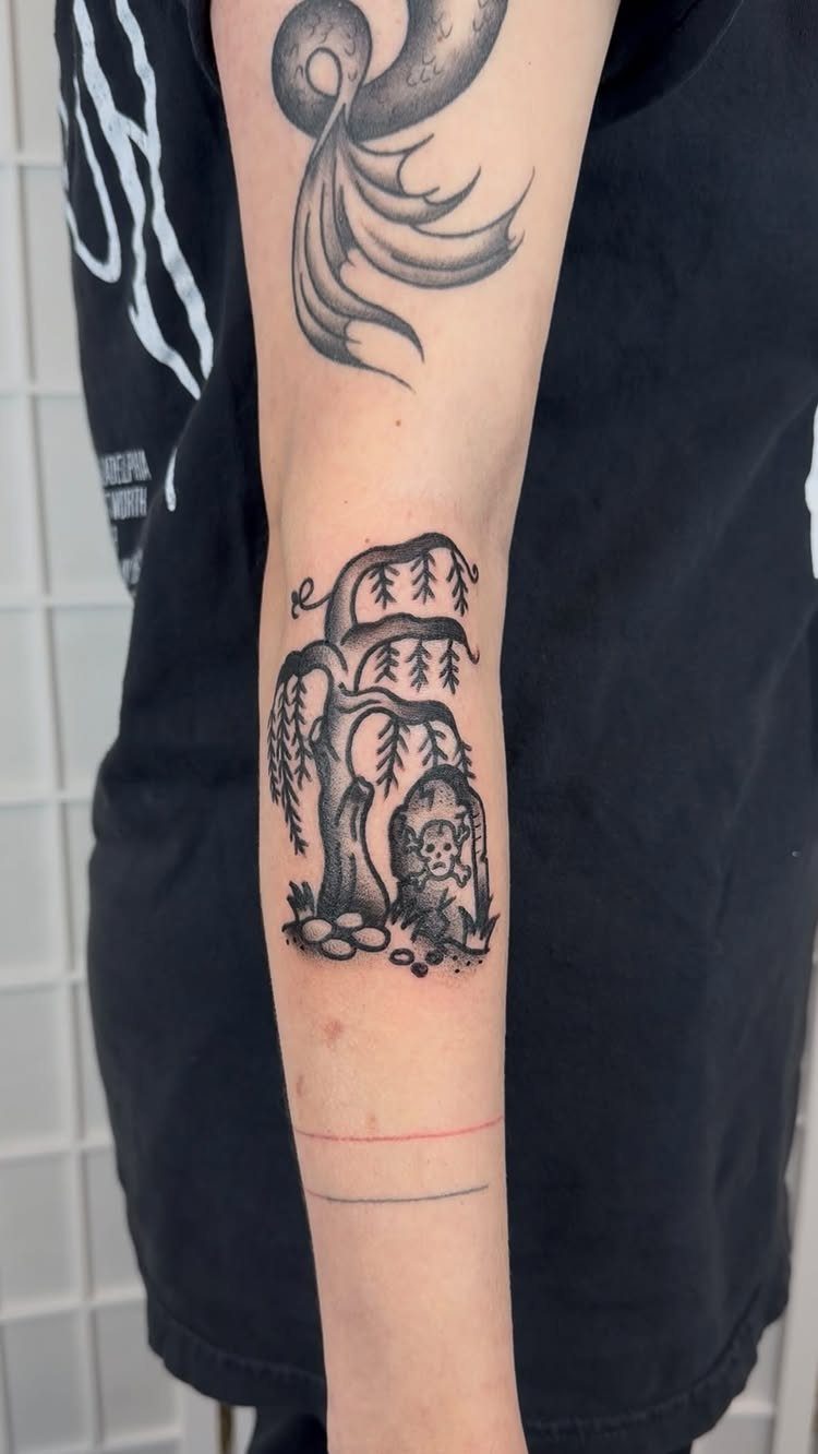 Willow tree tattoo with a gravestone and skull on a person's forearm.